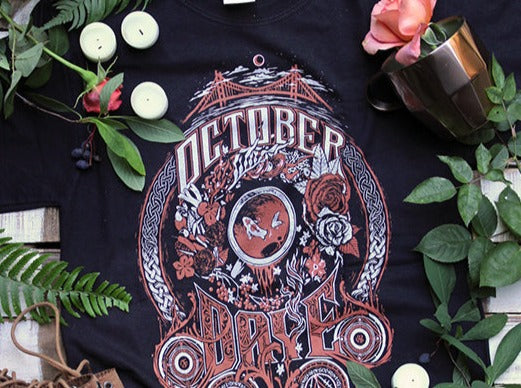 A black graphic tee shirt with a tyopgraphic illustration that reads "October Daye". The Illustration includes roses, koi, and other iconography from the book series October Daye by Seanan McGuire. 