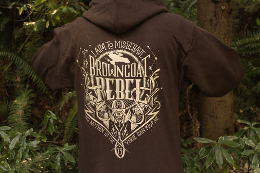 A person wearing a dark brown sweatshirt featuring a large distressed gold graphic print with the text 'I AM TO MISBEHAVE BROWNCOAT REBELLION' and illustrated details.