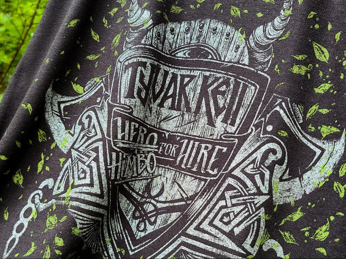 Close-up of a black graphic t-shirt featuring a distressed white and green print with the text "TYVAR KELL" - "HERO/HIMBO FOR HIRE"