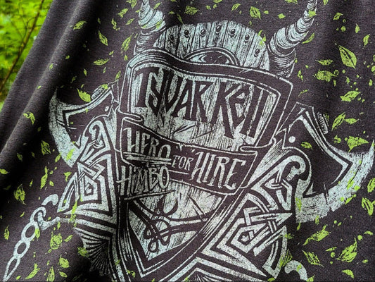 Close-up of a black graphic t-shirt featuring a distressed white and green print with the text "TYVAR KELL" - "HERO/HIMBO FOR HIRE"