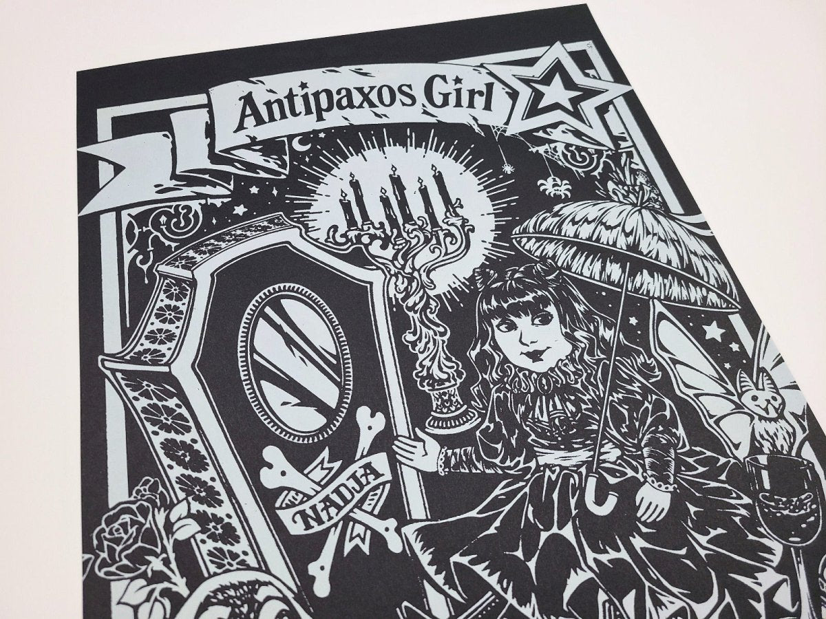Black and white illustration of a doll with an umbrella and decorative elements, featuring the text 'Antipaxos Girl'.