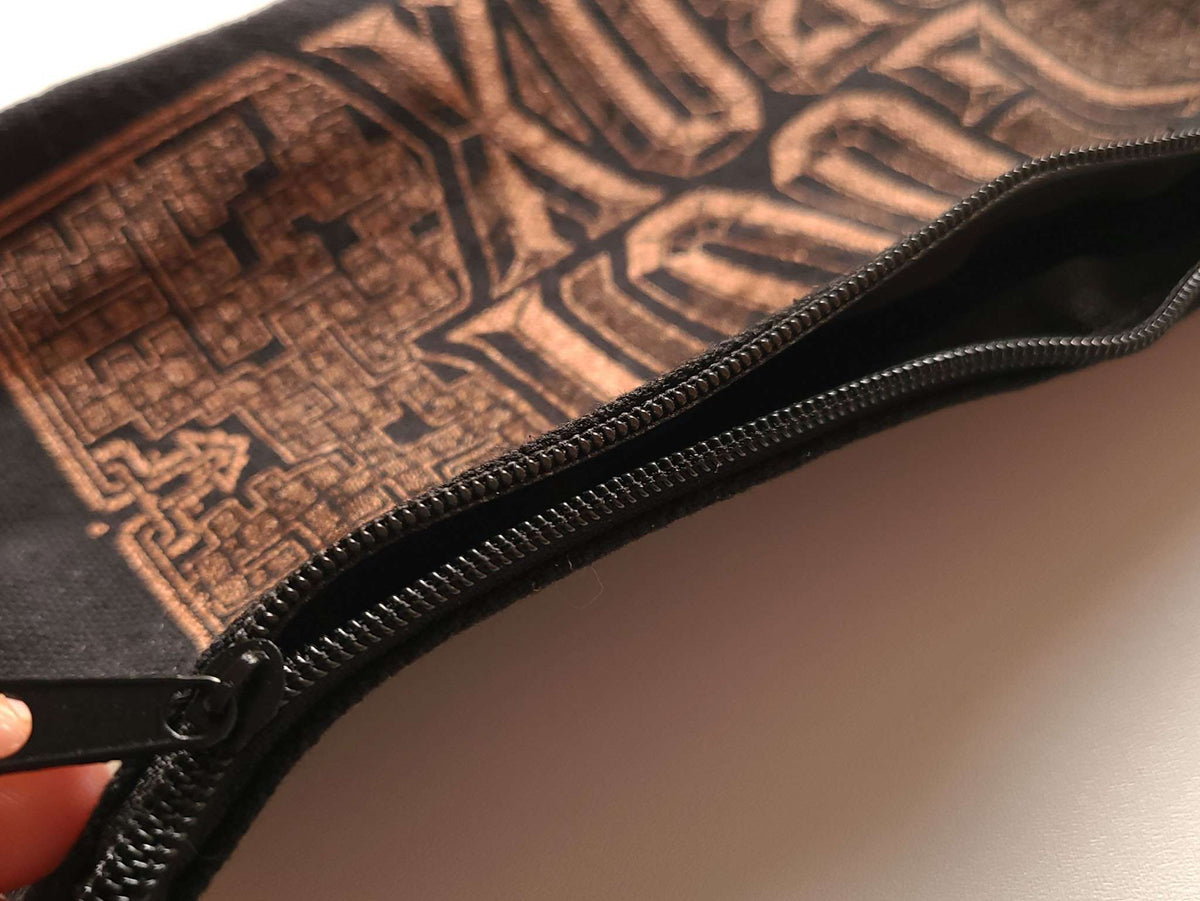 Close-up of a black zipper pouch with a copper and black geometric graphic pattern, held open by a hand.