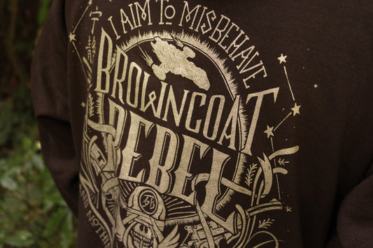 Close-up of a dark brown sweatshirt featuring a large distressed gold graphic print with the text 'I AM TO MISBEHAVE BROWNCOAT REBELLION' and illustrated details.