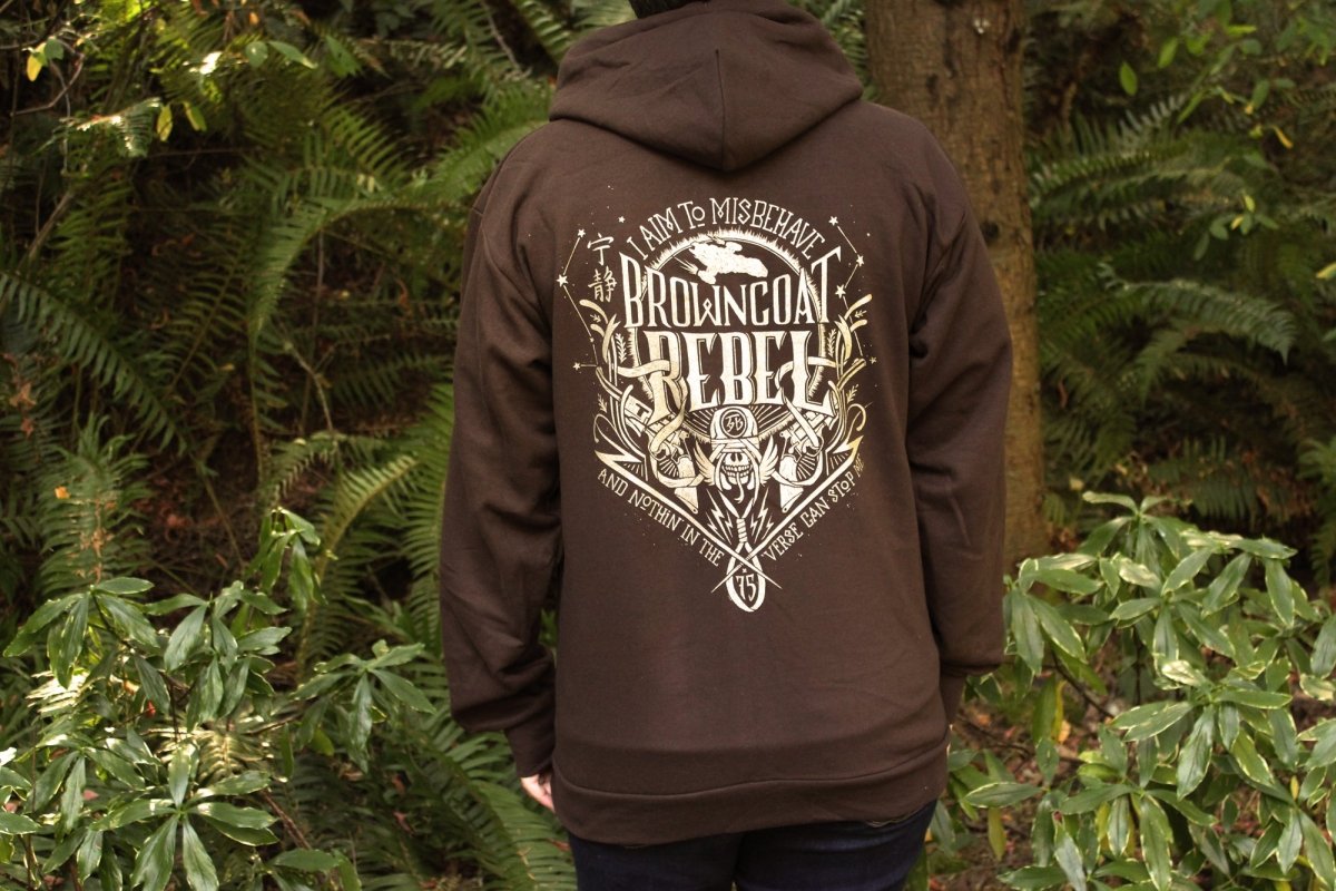 A person wearing a dark brown sweatshirt featuring a large distressed gold graphic print with the text 'I AM TO MISBEHAVE BROWNCOAT REBELLION' and illustrated details.