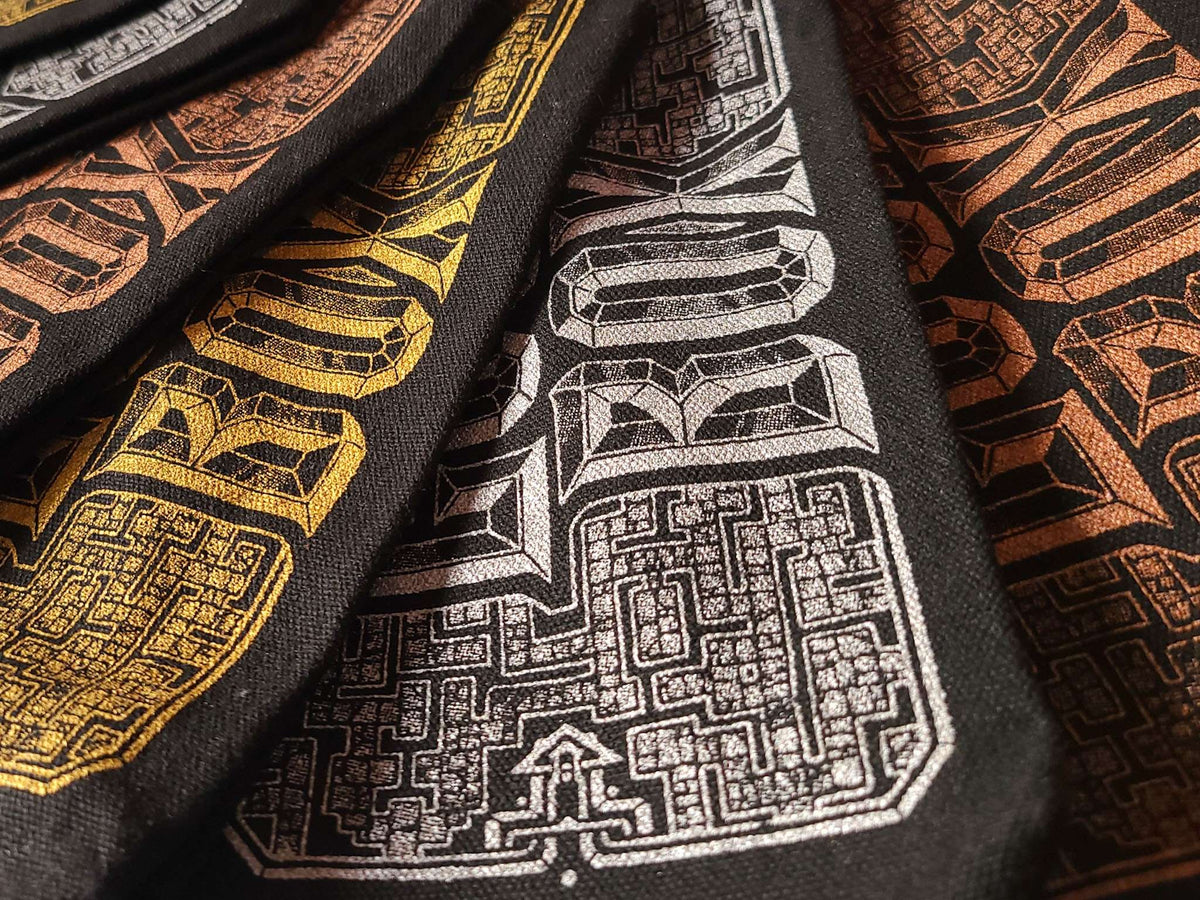 Close-up of black fabric makeup bags, featuring intricate geometric and maze-like patterns in white, gold, and copper-brown.